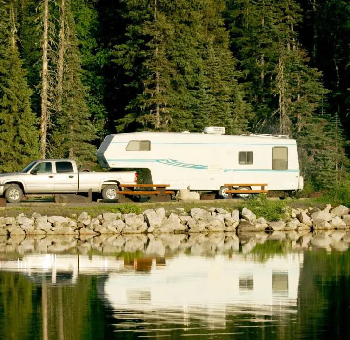 A truck and camper are parked on the side of a lake.