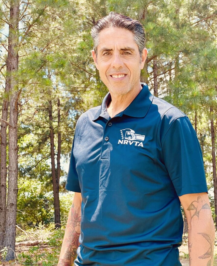 A man in blue shirt standing next to trees.